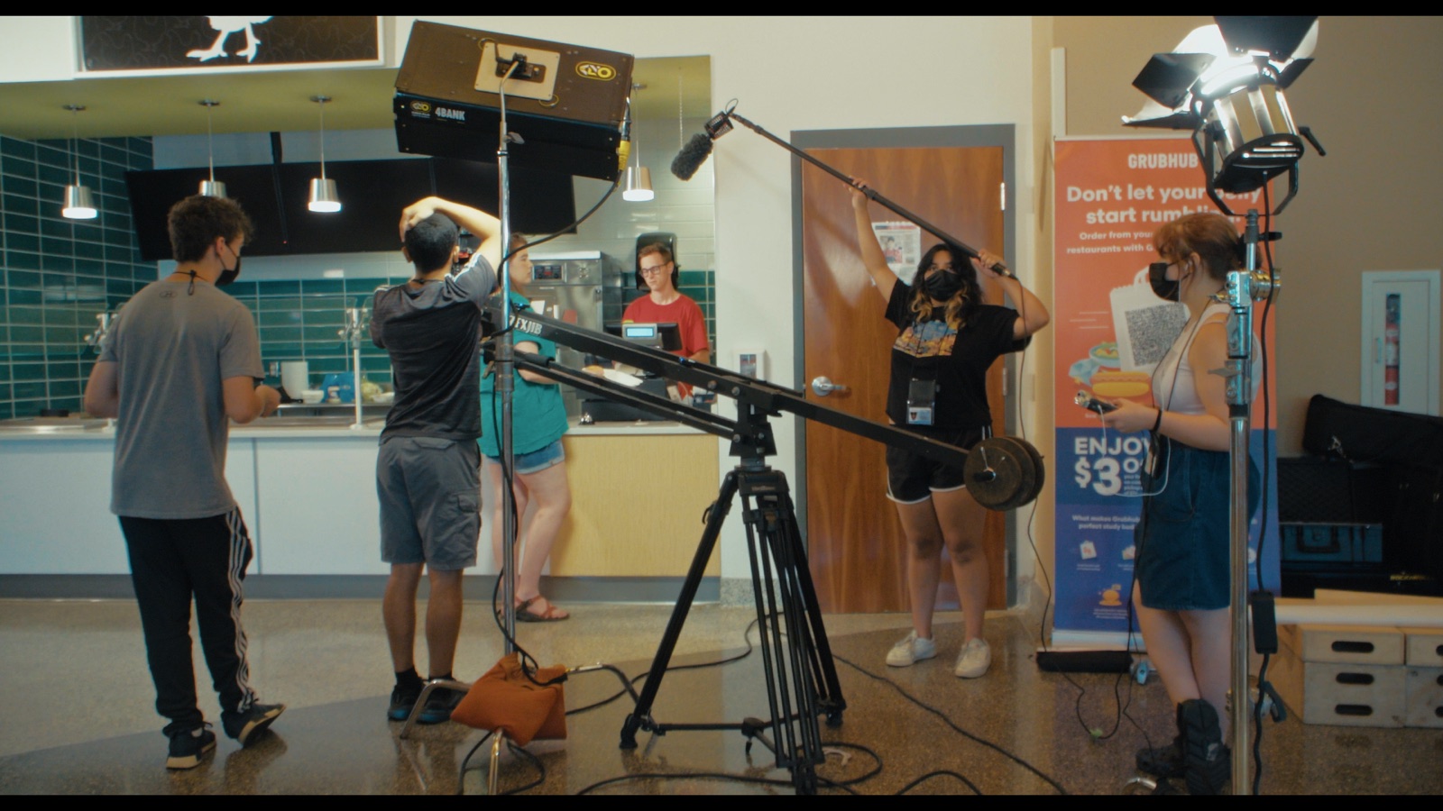 A student crew shooting in a dorm kitchen with a boom pole, a jib arm and a light stand