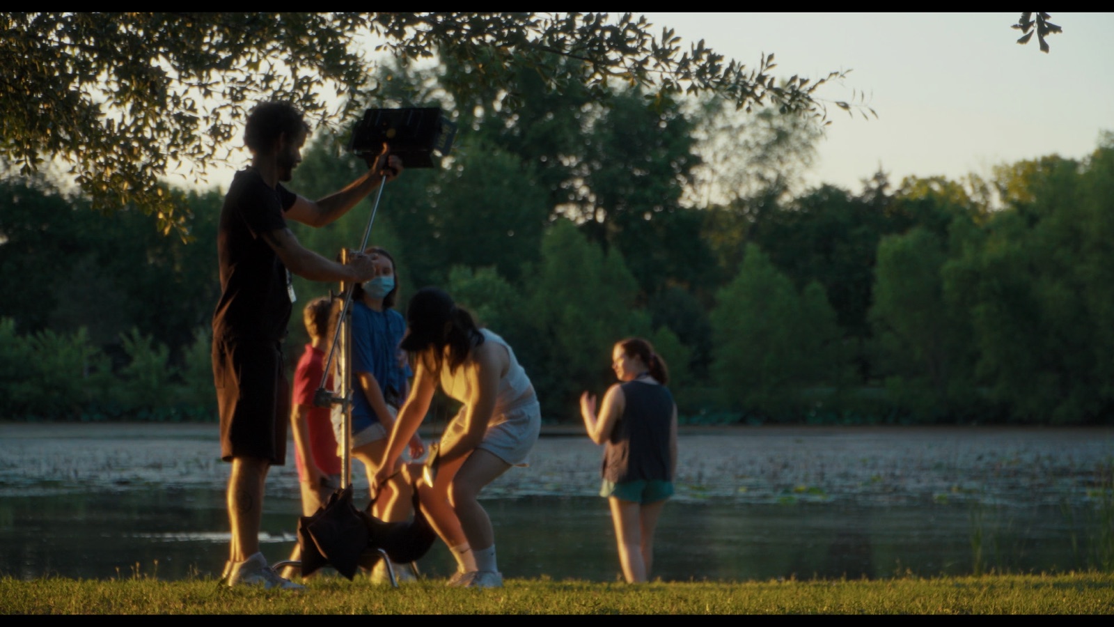 Students setting up a shot with a boom mic and lights beside a lake at dusk
