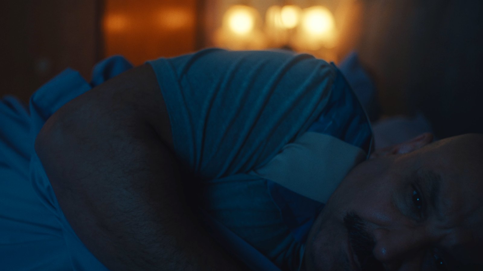 Luz's husband lying in bed, turned away, in blue night light