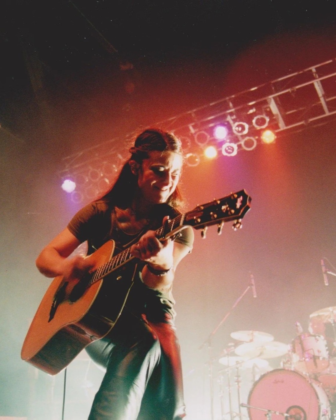 A performer playing acoustic guitar under colored stage lights