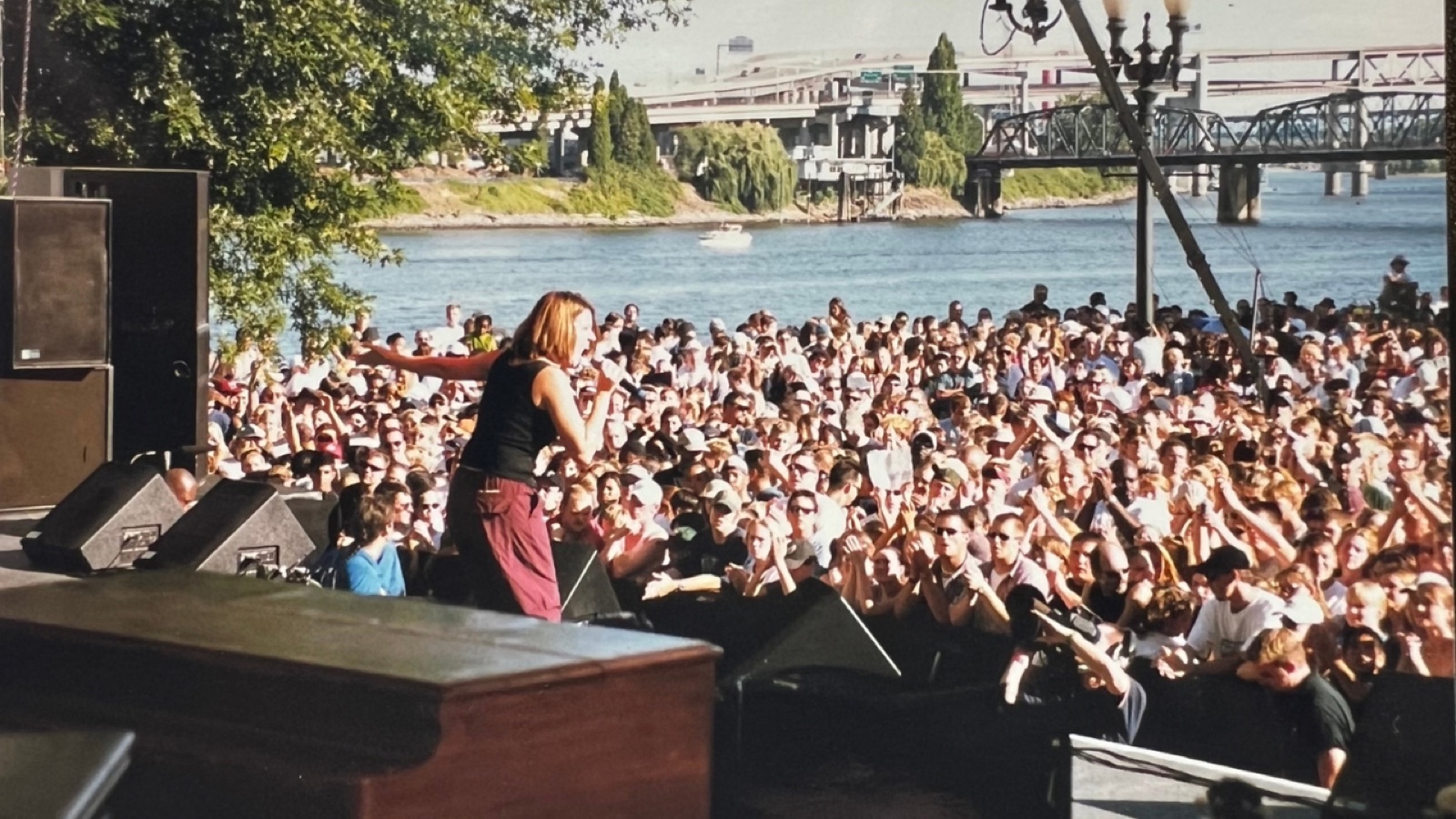 A singer performing on a riverside stage before a huge outdoor crowd
